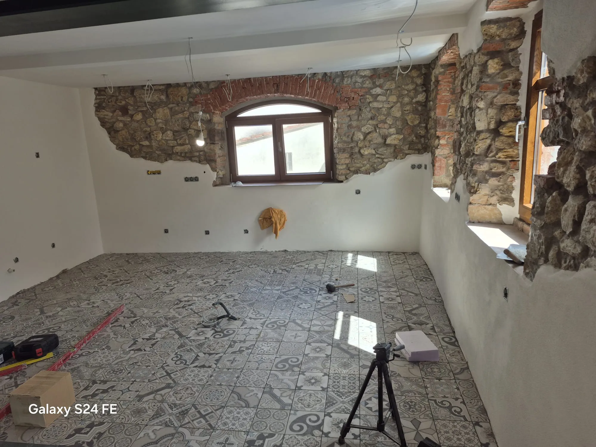 Raum mit freigelegter Natursteinwand, Ziegelbogen über dem Fenster und gemustertem Fliesenboden