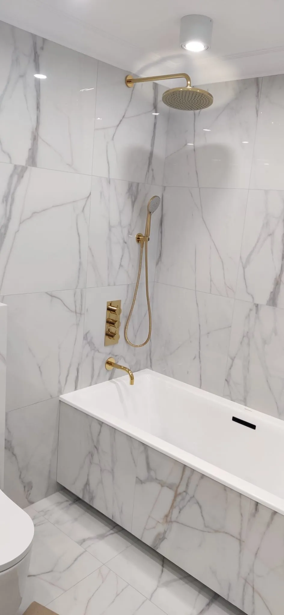 Badewanne mit Marmoroptik-Verkleidung, goldener Unterputzarmatur und Regenbrause