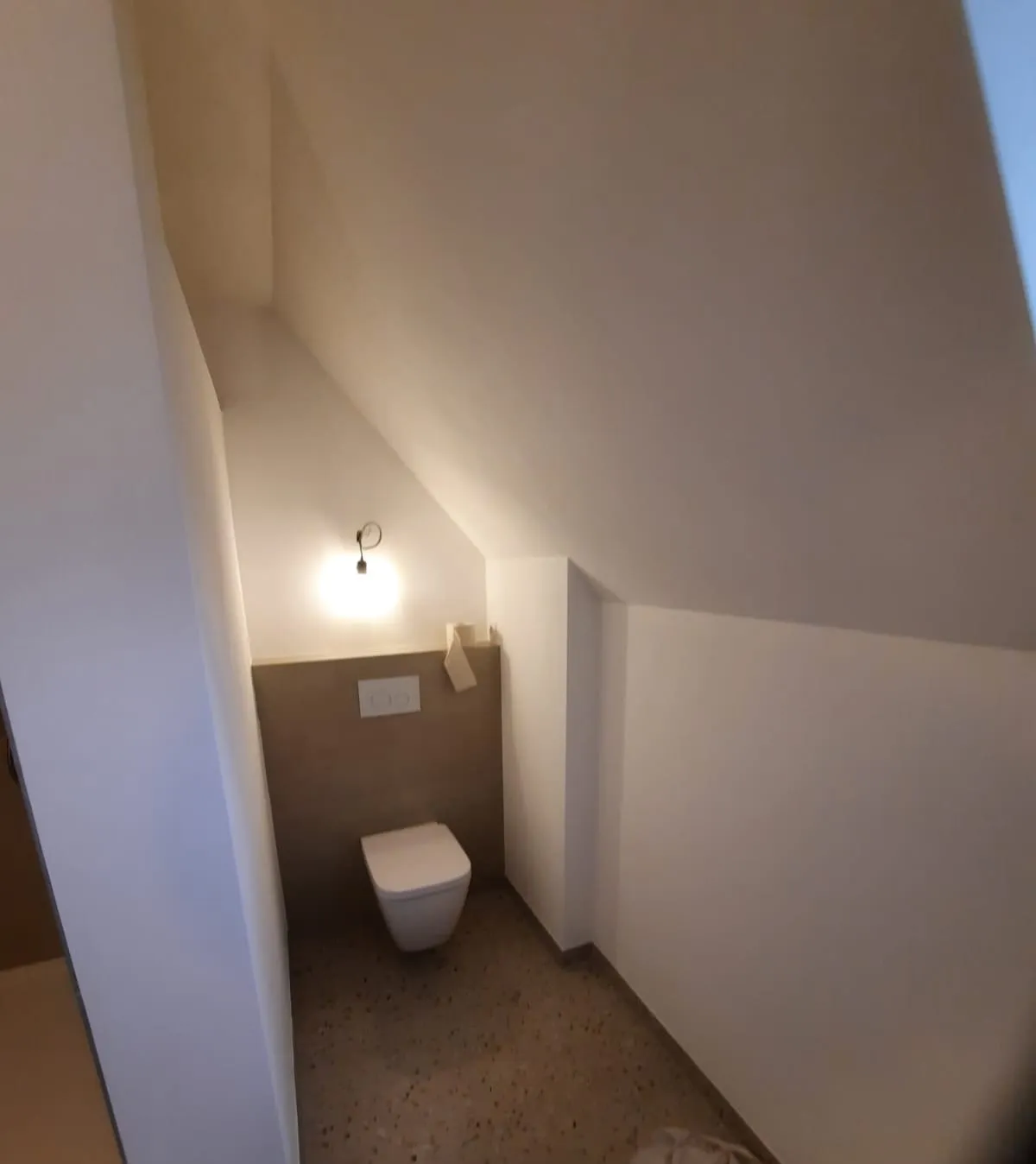 Wand-WC unter der Dachschräge mit halbhoher Fliesenwand und Wandleuchte
